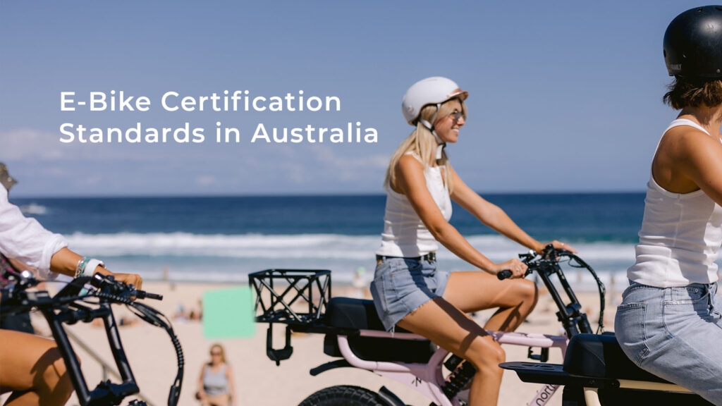 I'm of three woman riding e-bikes along a coastal promenade, with the text "E-Bike Certification Standards in Australia".